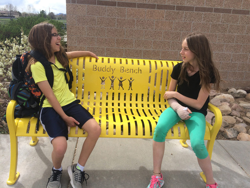 Two girls sit on a Buddy Bench