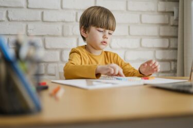kid writing and coloring a piece of paper, sitting at a desk