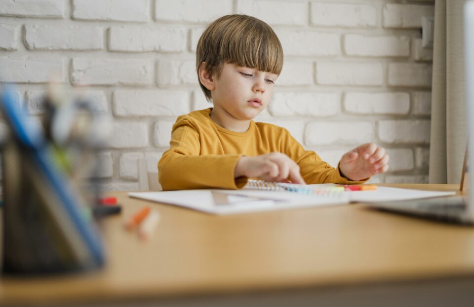 kid writing and coloring a piece of paper, sitting at a desk